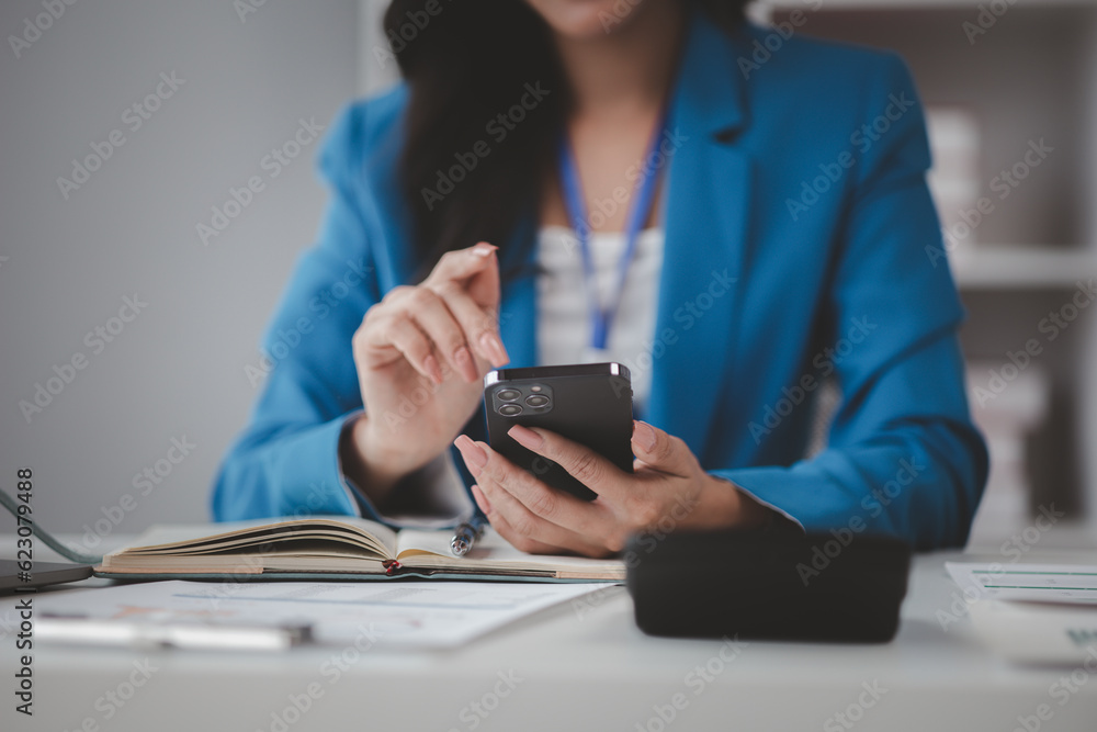 Fototapeta premium Beautiful asian woman looking at data on phone, businesswoman working in office attentively to grow and modernize start-up business, she is analyzing company's market and financial data.