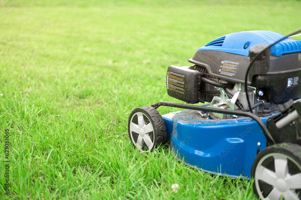 Fototapeta premium Lawn mower cutting grass. Small grass cuttings fly out of lawnmower. Grass clippings get spewed out of a mower pushed around by landscaper. Slow Motion. CloseUp. Gardener working with mower machine.