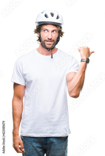 Handsome hispanic cyclist man wearing safety helmet over isolated background smiling with happy face looking and pointing to the side with thumb up.