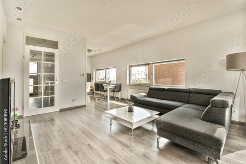 a living room with wood flooring and white walls  there is a black couch in the center of the room