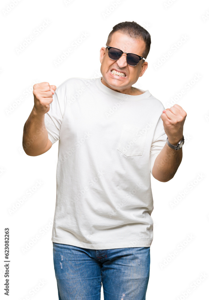 Naklejka premium Middle age arab man wearig white t-shirt and sunglasses over isolated background very happy and excited doing winner gesture with arms raised, smiling and screaming for success. Celebration concept.