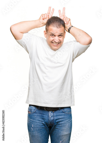 Middle age arab man wearig white t-shirt over isolated background Posing funny and crazy with fingers on head as bunny ears, smiling cheerful