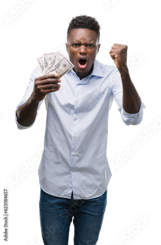 Young african american businessman holding dollars annoyed and frustrated shouting with anger, crazy and yelling with raised hand, anger concept