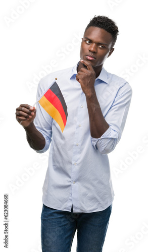 Young african american man holding german flag serious face thinking about question, very confused idea