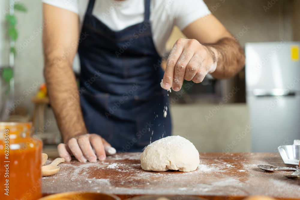 Happy cheerful Italian chef making a fresh pizza dough on wooden table in kitchen.