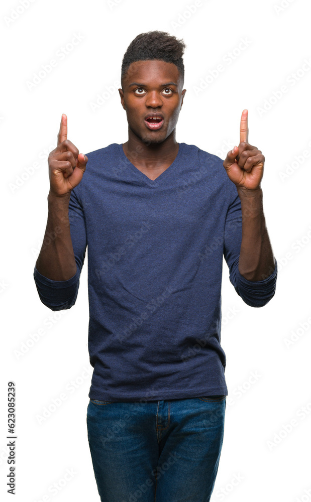 Young african american man over isolated background amazed and surprised looking up and pointing with fingers and raised arms. Young african american man over isolated background amazed and surprised looking up and pointing with fingers and raised arms.