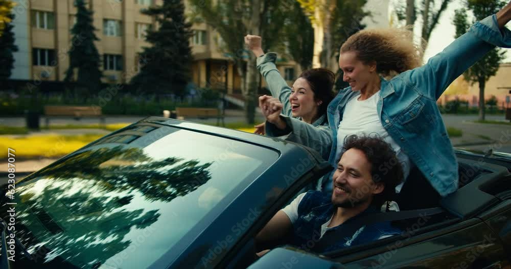 A happy trio: a guy and two girls are riding in a gray convertible. A blonde girl and a brunette girl have fun and rejoice. Happy cabriolet ride A happy trio: a guy and two girls are riding in a gray convertible. A blonde girl and a brunette girl have fun and rejoice. Happy cabriolet ride