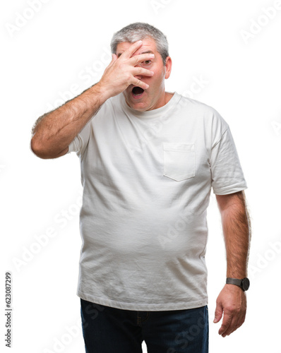 Handsome senior man over isolated background peeking in shock covering face and eyes with hand, looking through fingers with embarrassed expression.
