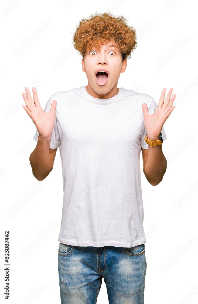 Young handsome man with afro hair wearing casual white t-shirt celebrating crazy and amazed for success with arms raised and open eyes screaming excited. Winner concept Young handsome man with afro hair wearing casual white t-shirt celebrating crazy and amazed for success with arms raised and open eyes screaming excited. Winner concept