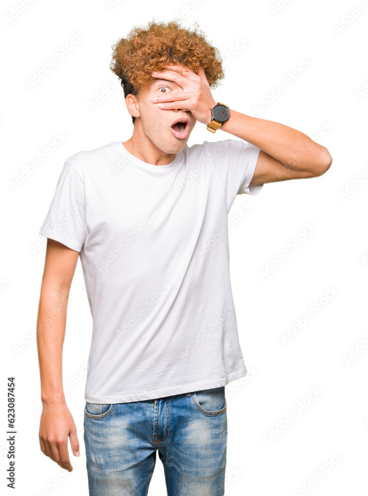 Young handsome man with afro hair wearing casual white t-shirt peeking in shock covering face and eyes with hand, looking through fingers with embarrassed expression. Young handsome man with afro hair wearing casual white t-shirt peeking in shock covering face and eyes with hand, looking through fingers with embarrassed expression.