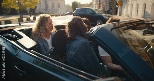 Happy friends in a dark gray convertible have arrived at their destination and are parking their car, they are chatting and having fun