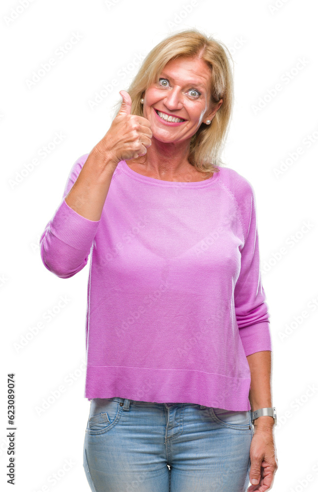 Middle age blonde woman over isolated background doing happy thumbs up gesture with hand. Approving expression looking at the camera with showing success. Middle age blonde woman over isolated background doing happy thumbs up gesture with hand. Approving expression looking at the camera with showing success.