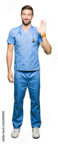 Handsome doctor man wearing medical uniform over isolated background Waiving saying hello happy and smiling, friendly welcome gesture