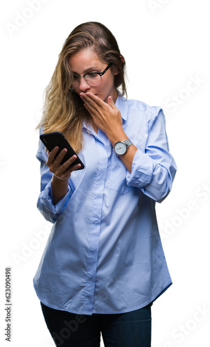 Young beautiful blonde business woman using smartphone over isolated background cover mouth with hand shocked with shame for mistake, expression of fear, scared in silence, secret concept © Krakenimages.com
