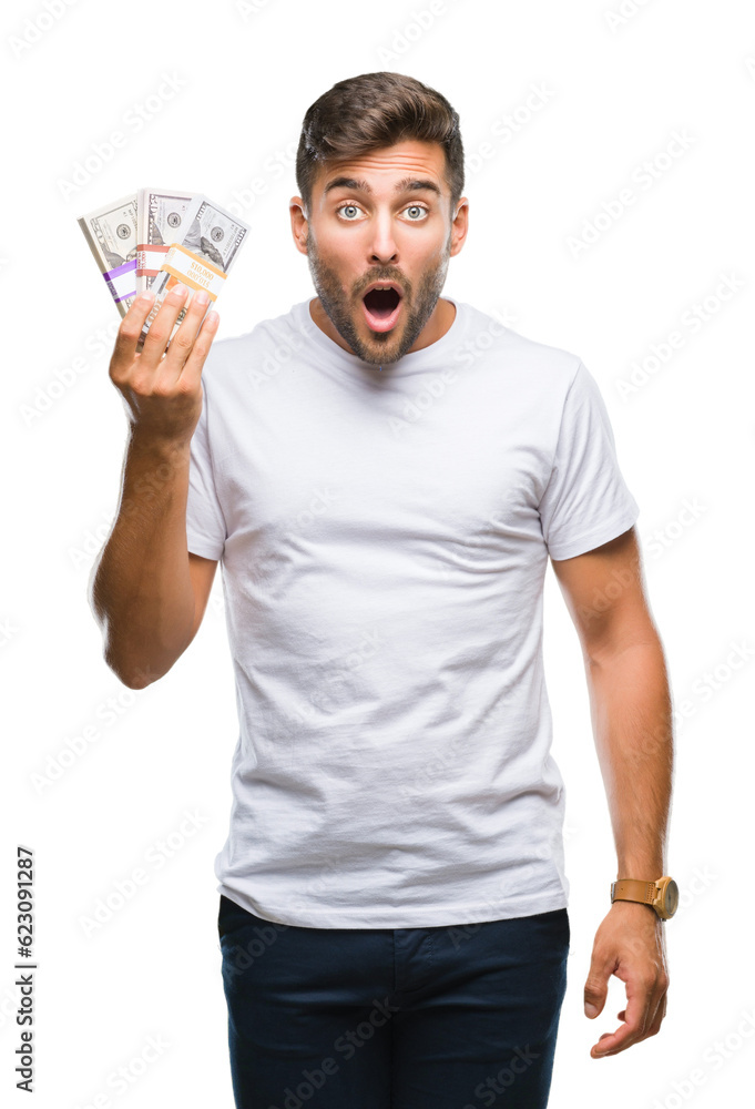 Young handsome man holding stack of dollars over isolated background scared in shock with a surprise face, afraid and excited with fear expression Young handsome man holding stack of dollars over isolated background scared in shock with a surprise face, afraid and excited with fear expression