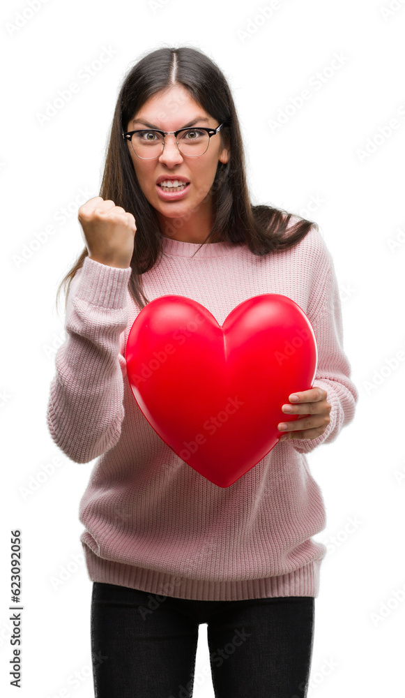 Young hispanic woman holding heart in love annoyed and frustrated shouting with anger, crazy and yelling with raised hand, anger concept Young hispanic woman holding heart in love annoyed and frustrated shouting with anger, crazy and yelling with raised hand, anger concept