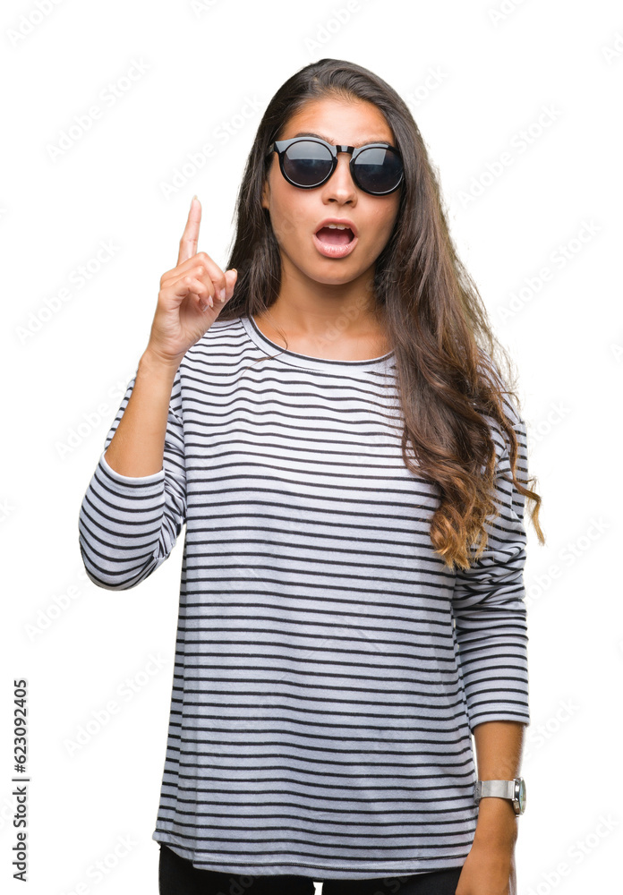 Naklejka premium Young beautiful arab woman wearing sunglasses over isolated background pointing finger up with successful idea. Exited and happy. Number one.