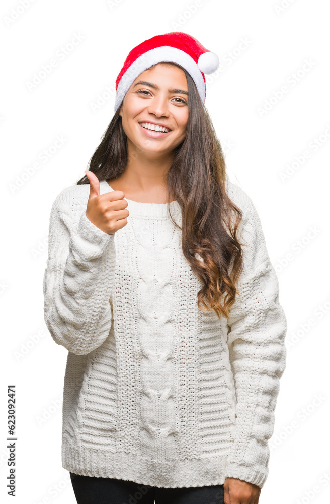 Young arab woman wearing christmas hat over isolated background doing happy thumbs up gesture with hand. Approving expression looking at the camera with showing success.