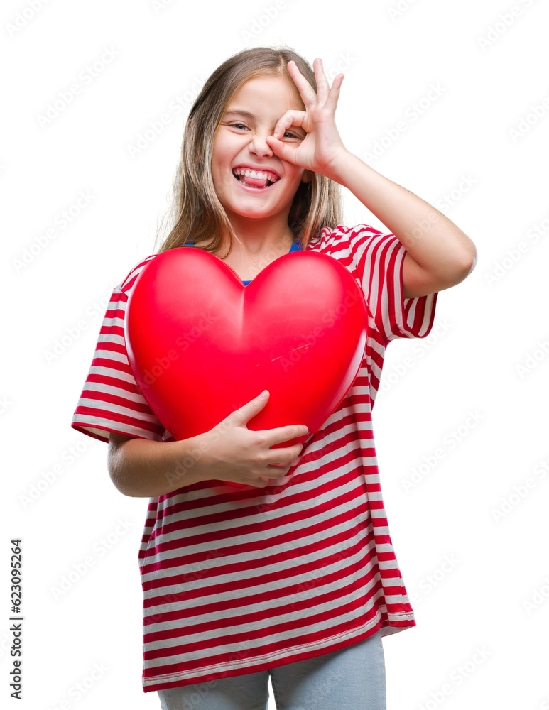 Young beautiful girl holding red heart over isolated background with happy face smiling doing ok sign with hand on eye looking through fingers Young beautiful girl holding red heart over isolated background with happy face smiling doing ok sign with hand on eye looking through fingers