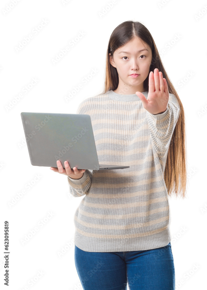 Young Chinese woman over isolated background using computer laptop with open hand doing stop sign with serious and confident expression, defense gesture Young Chinese woman over isolated background using computer laptop with open hand doing stop sign with serious and confident expression, defense gesture