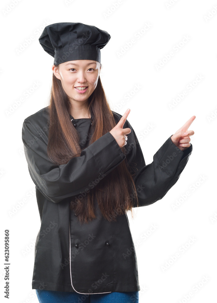 Young Chinese woman over isolated background wearing chef uniform smiling and looking at the camera pointing with two hands and fingers to the side. Young Chinese woman over isolated background wearing chef uniform smiling and looking at the camera pointing with two hands and fingers to the side.