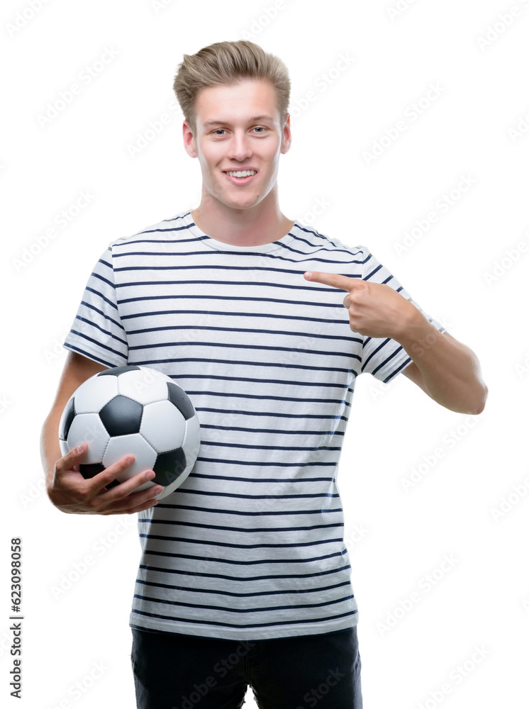 Young handsome blond man holding soccer ball with surprise face pointing finger to himself Young handsome blond man holding soccer ball with surprise face pointing finger to himself