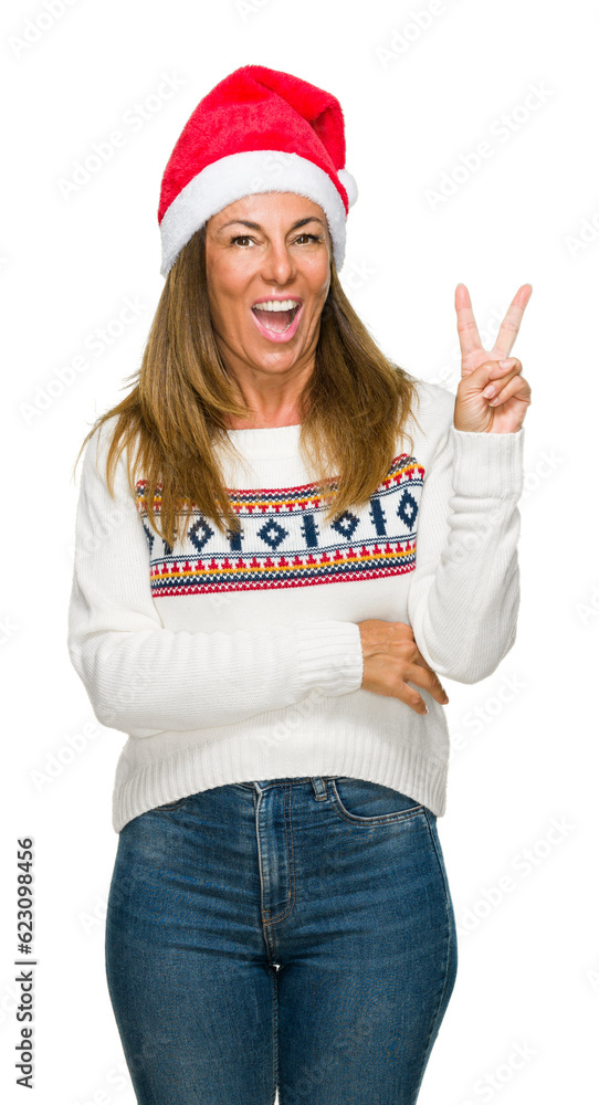 Middle age adult woman wearing winter sweater and chrismat hat over isolated background smiling with happy face winking at the camera doing victory sign. Number two. Middle age adult woman wearing winter sweater and chrismat hat over isolated background smiling with happy face winking at the camera doing victory sign. Number two.