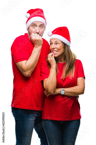 Middle age hispanic couple wearing christmas hat over isolated background looking stressed and nervous with hands on mouth biting nails. Anxiety problem.