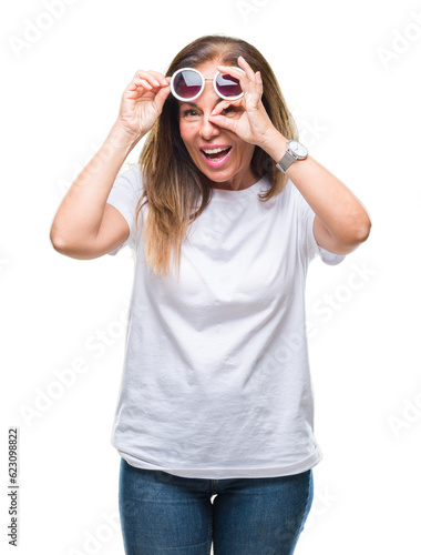 Middle age hispanic woman wearing fashion sunglasses over isolated background doing ok gesture with hand smiling, eye looking through fingers with happy face.
