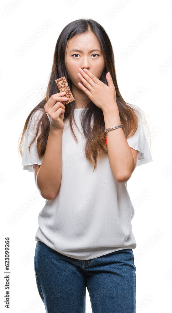 Young asian woman eating chocolate energetic bar over isolated background cover mouth with hand shocked with shame for mistake, expression of fear, scared in silence, secret concept Young asian woman eating chocolate energetic bar over isolated background cover mouth with hand shocked with shame for mistake, expression of fear, scared in silence, secret concept