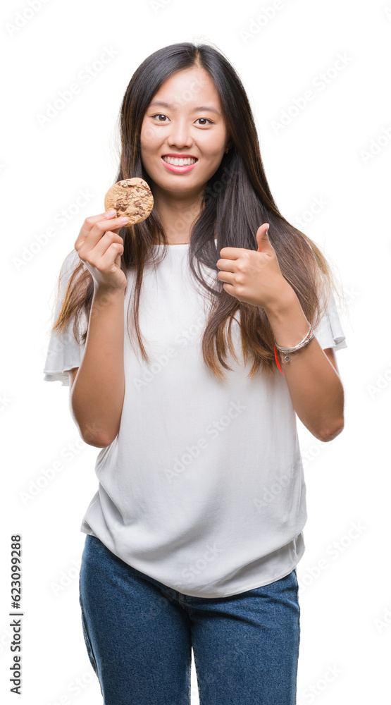Young asian woman eating chocolate chip cookie over isolated background happy with big smile doing ok sign, thumb up with fingers, excellent sign Young asian woman eating chocolate chip cookie over isolated background happy with big smile doing ok sign, thumb up with fingers, excellent sign