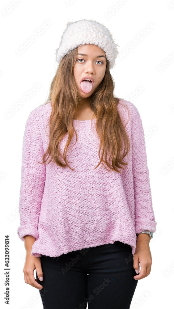 Young beautiful brunette woman wearing sweater and winter hat over isolated background sticking tongue out happy with funny expression. Emotion concept. Young beautiful brunette woman wearing sweater and winter hat over isolated background sticking tongue out happy with funny expression. Emotion concept.