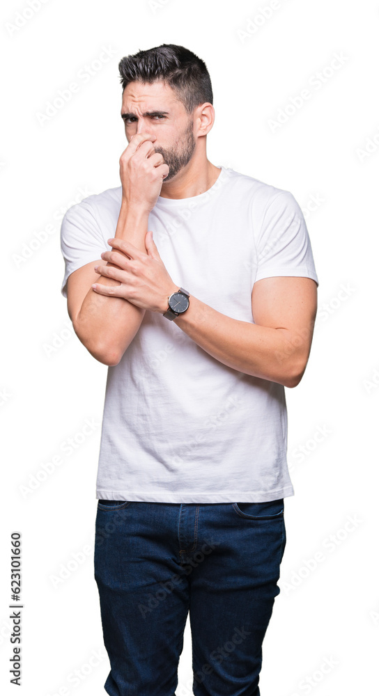 Young man wearing casual white t-shirt over isolated background smelling something stinky and disgusting, intolerable smell, holding breath with fingers on nose. Bad smells concept. Young man wearing casual white t-shirt over isolated background smelling something stinky and disgusting, intolerable smell, holding breath with fingers on nose. Bad smells concept.