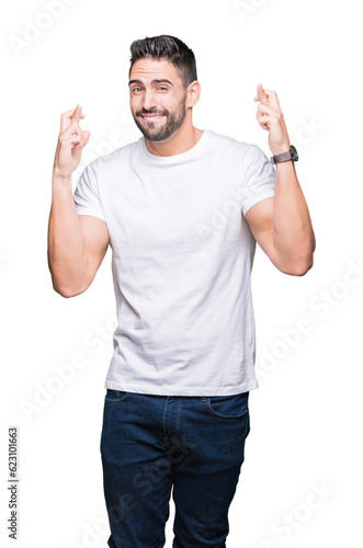 Young man wearing casual white t-shirt over isolated background smiling crossing fingers with hope and eyes closed. Luck and superstitious concept.