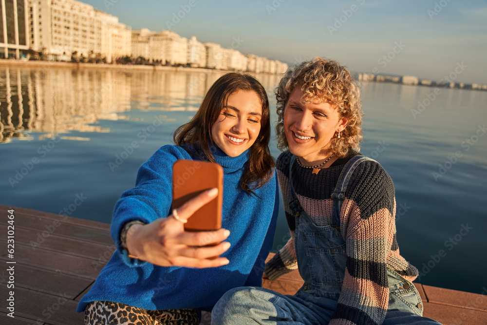 Lovely friends holding smartphone and taking self portrait a the lake background