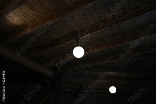 2 Round bulbs lighting in the dark room or basement. A light bulb hangs on a wooden beam. Two lights in the ceiling that illuminate the dark corridor 