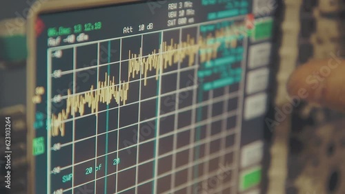 hand held close up shot of spectrum analyzer screen with megahertz decibels and other readings, finger push buttons