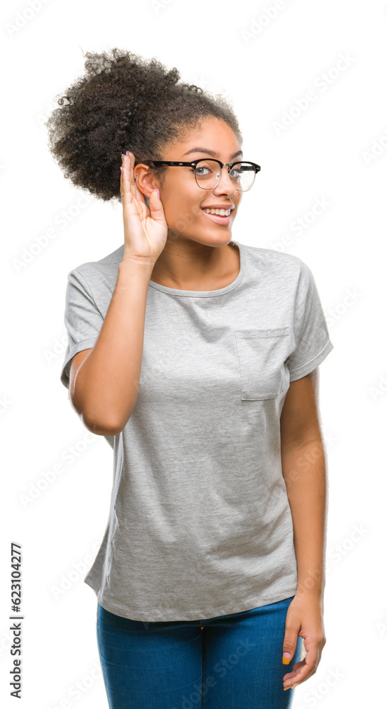Young afro american woman wearing glasses over isolated background smiling with hand over ear listening an hearing to rumor or gossip. Deafness concept.