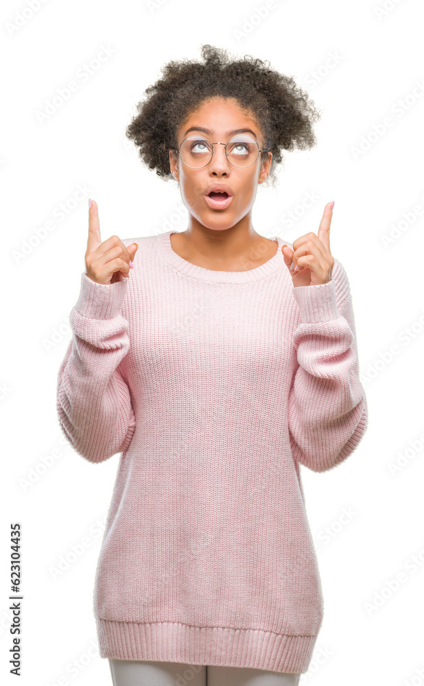 Young afro american woman wearing glasses over isolated background amazed and surprised looking up and pointing with fingers and raised arms. Young afro american woman wearing glasses over isolated background amazed and surprised looking up and pointing with fingers and raised arms.