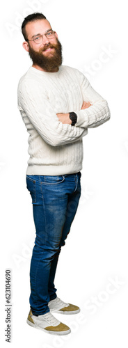 Young hipster man wearing glasses and winter sweater happy face smiling with crossed arms looking at the camera. Positive person.