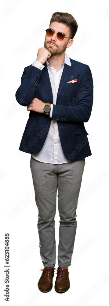 Young handsome elegant man wearing sunglasses and fashion blazer with hand on chin thinking about question, pensive expression. Smiling with thoughtful face. Doubt concept. Young handsome elegant man wearing sunglasses and fashion blazer with hand on chin thinking about question, pensive expression. Smiling with thoughtful face. Doubt concept.