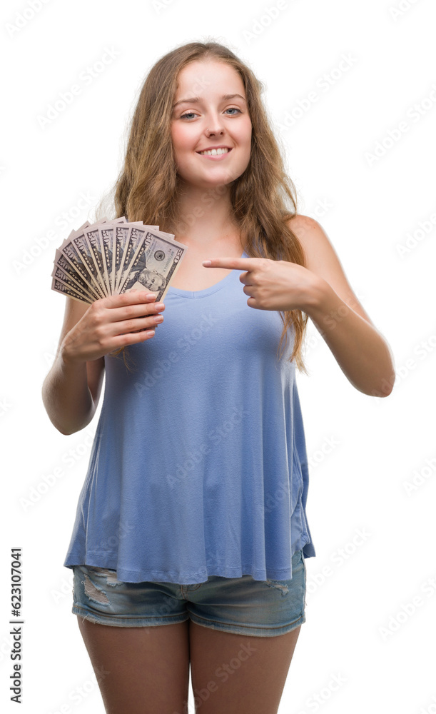 Young blonde woman holding dollars very happy pointing with hand and finger Young blonde woman holding dollars very happy pointing with hand and finger