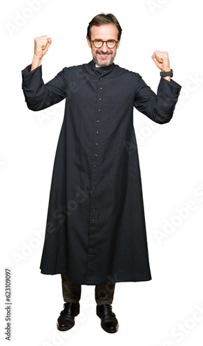 Middle age priest man wearing catholic robe showing arms muscles smiling proud. Fitness concept.