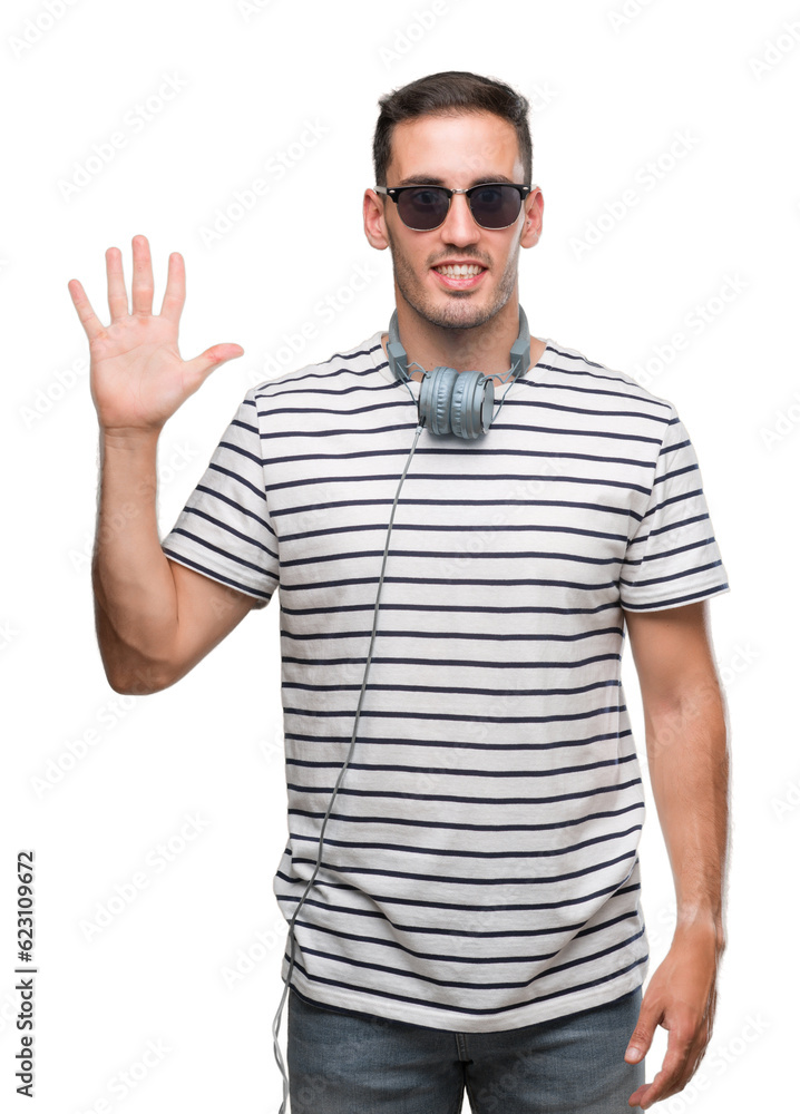 Handsome young man wearing headphones showing and pointing up with fingers number five while smiling confident and happy. Handsome young man wearing headphones showing and pointing up with fingers number five while smiling confident and happy.