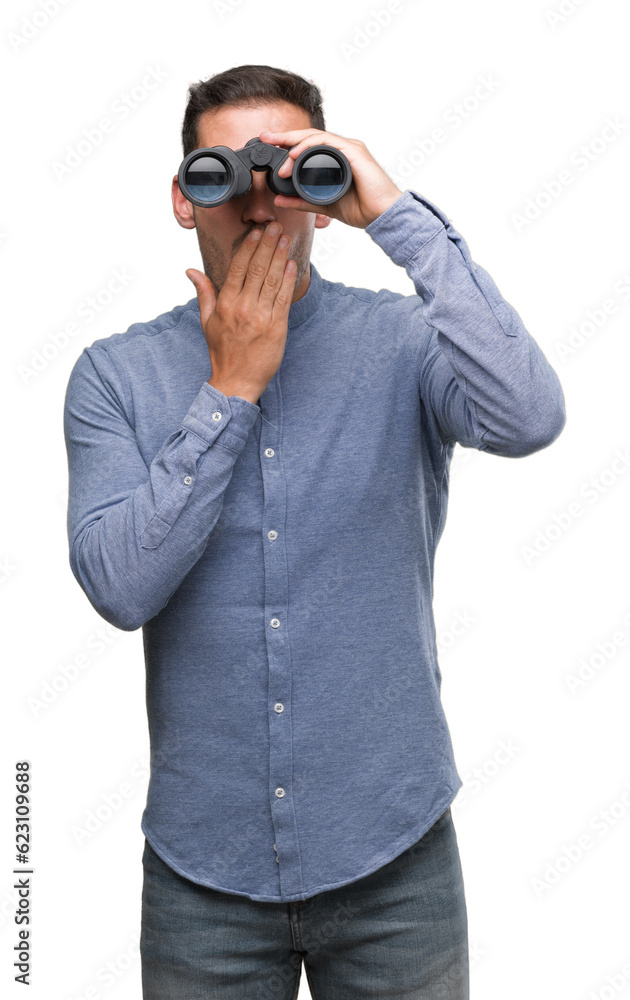 Handsome young man looking through binoculars cover mouth with hand shocked with shame for mistake, expression of fear, scared in silence, secret concept