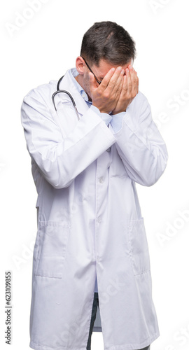 Handsome young doctor man with sad expression covering face with hands while crying. Depression concept.