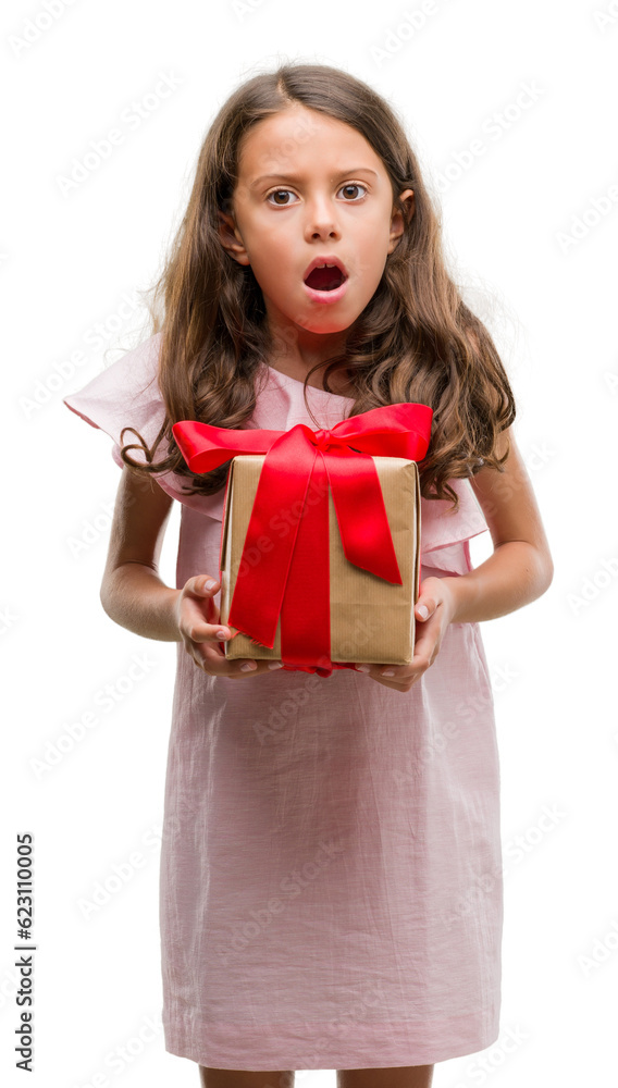 Brunette hispanic girl holding a gift scared in shock with a surprise face, afraid and excited with fear expression Brunette hispanic girl holding a gift scared in shock with a surprise face, afraid and excited with fear expression