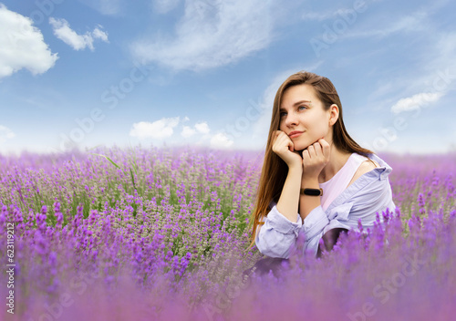 A young Ukrainian woman is sitting on a lavender field dreaming, blue cloudy sky. Nature of Ukraine, countryside. Real photo