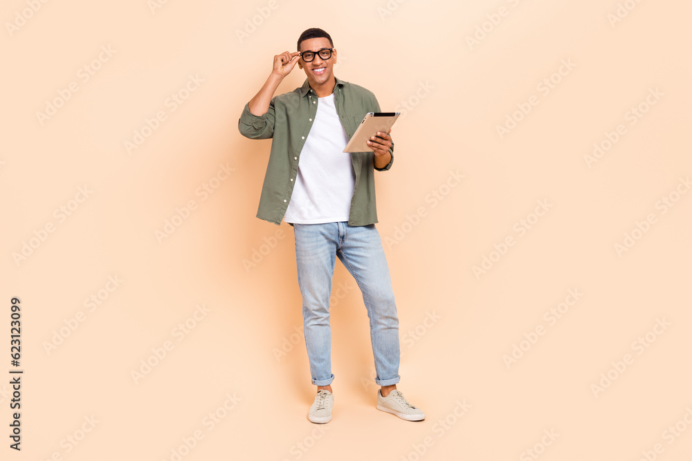 Full size photo of friendly positive man hold use tablet hand touch eyeglasses isolated on beige color background Full size photo of friendly positive man hold use tablet hand touch eyeglasses isolated on beige color background