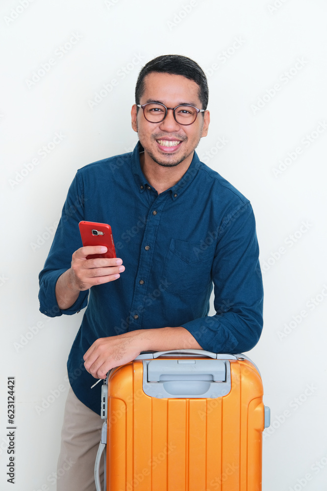 Adult Asian man smiling confident holding mobile phone posing in front of his baggage Adult Asian man smiling confident holding mobile phone posing in front of his baggage